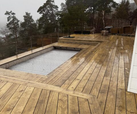 Rengjord altan med breda trappsteg runt en täckt pool och glasräcke.
