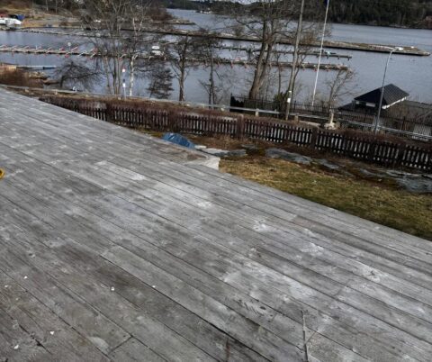 Stor, grå träaltan med sjöutsikt och ett träräcke längre ned i trädgården.
