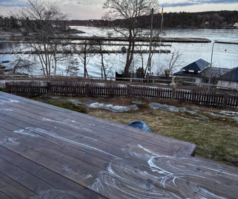 Våt träaltan med skum på trallbrädorna och utsikt mot vatten.
