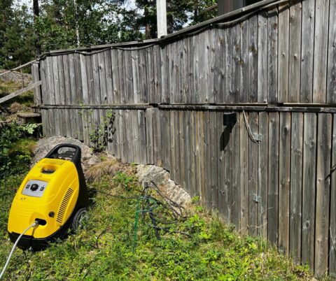 Väderbitet träräcke ovanför berg och gräs före rengöring.