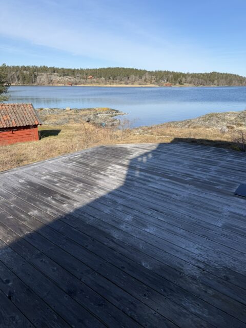 Grå träaltan med utsikt över vatten och klippor före rengöring.
